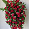 Tall standing spray of red flowers with greenery on a black easel