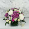 Pink and white rose bouquet in a square glass vase with a small candle beside it.
