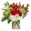 Red roses and lilies arranged with white hydrangeas in a glass vase