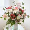 Bouquet of white daisies, pink roses, and red berries in a glass vase