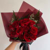 Handheld bouquet of red roses wrapped in burgundy paper