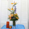 Tall tropical flower arrangement in a clear glass vase with orange and blue blooms