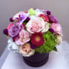 Mixed pink, purple, and white flowers arranged in a round box