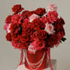 Large bouquet of red and pink roses in a red hatbox with pearl strands