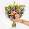 Handheld bouquet of mixed pastel flowers wrapped in brown paper