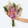 Handheld bouquet of pink and peach roses with mixed blooms wrapped in paper