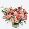 Mixed pink and peach flowers arranged in a clear glass vase