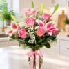 Pink roses and lilies arranged in a clear glass vase with a pink ribbon.