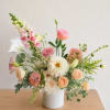Pastel floral arrangement in a white vase with pink and cream blooms