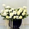 White floral arrangement in a dark vase with trailing white strands