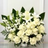 White floral arrangement in a woven basket with dark green leaves