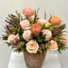 Peach and blush roses with orange ranunculus in a rustic vase
