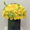 Dense arrangement of yellow and white roses with green blooms in a tall dark green cylinder vase