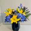 Blue hydrangeas and yellow lilies arranged in a dark vase