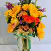 Bright mixed bouquet with sunflowers and roses in a clear glass vase
