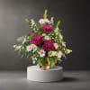Pink and white flower arrangement in a gold vase on a pedestal