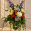 Tall mixed bouquet in a glass vase with purple, blue, white, and orange flowers
