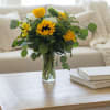Yellow and white flowers in a clear glass vase on a coffee table