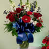 Red roses and white flowers in a glass vase with a blue ribbon