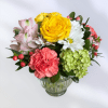 Mixed bouquet of yellow roses, pink flowers, white daisies, and green hydrangea in a glass vase