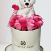 White teddy bear sitting in a box of pink roses with a ribbon