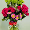 Pink roses and mixed daisies in a clear glass vase with a red ribbon