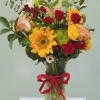 Mixed bouquet of sunflowers, red roses, and lilies in a glass vase with a red ribbon