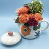 Orange and magenta roses arranged in a floral teapot with a matching lid.