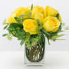 Yellow roses arranged in a clear glass vase with greenery