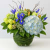 Bouquet of blue irises, pale hydrangea, and lime roses in a glass vase