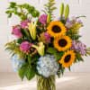 Mixed bouquet with sunflowers, roses, lilies, and hydrangeas in a glass vase