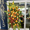 Tall floral standing spray with oranges, sunflowers, and peach roses