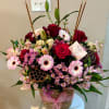 Mixed pink and red flower arrangement in a woven basket with a ribbon