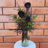 Black roses arranged in a clear glass vase with dark foliage