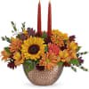 With its shimmering, copper-hued bowl, radiant mix of sunflowers and glowing tapers