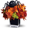 A googly-eyed spider sits atop a beautiful bouquet of orange roses, orange