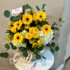 Yellow gerbera daisies and roses in a glass vase with greenery