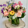 Mixed bouquet in a green glass vase with pink, purple, blue, and yellow flowers