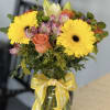 Bouquet of yellow gerbera daisies and peach roses in a glass vase with a yellow ribbon