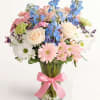 Mixed bouquet of pastel flowers in a glass vase with a pink ribbon