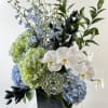 Blue and green floral arrangement with white orchids in a black vase