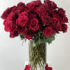 Bouquet of red roses in a clear glass vase with petals around the base