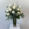 White roses arranged in a tall glass vase with eucalyptus foliage