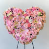 Heart-shaped pink floral arrangement with roses, carnations, and lilies on a stand
