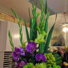 Tall floral arrangement with purple orchids and green blooms in a black container