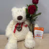 White teddy bear beside two red roses in a glass vase and a Dunkin' gift card