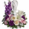 White angel figurine surrounded by purple, pink, and white flowers