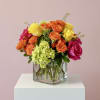 Bouquet of orange, yellow, and pink roses in a clear square vase