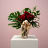 Arrangement of red roses with large glossy leaves in a glass vase tied with a gold bow