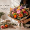 Hand-tied bouquet of peach, pink, and purple flowers wrapped in paper
